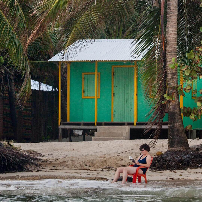 3 Tips For A Relaxed And Optimistic Life Through Meditation - person reading by ocean near colorful house