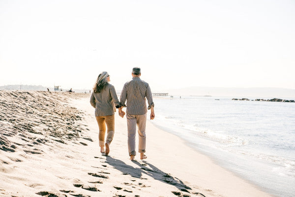 Couple walking hand in hand on a beach during winter, boosting their winter wellness.