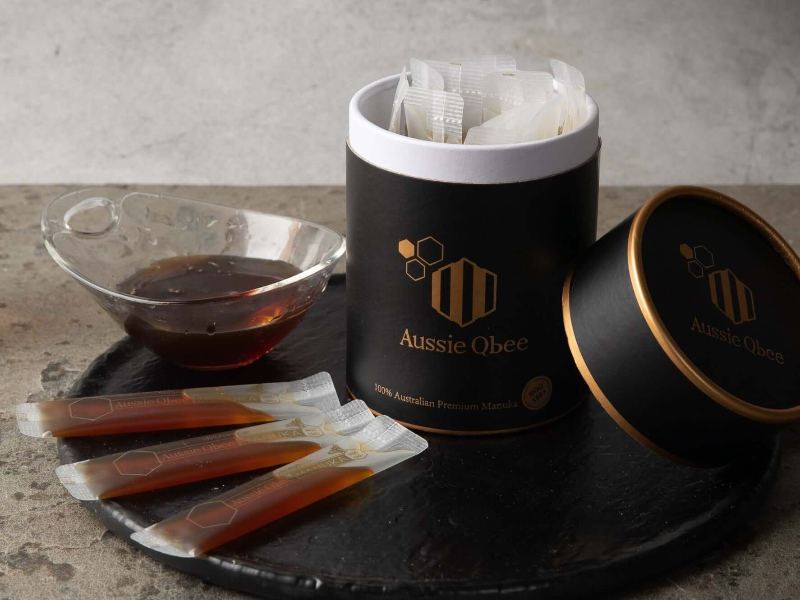 Aussie Qbee tea packaging with tea bags and a bowl of liquid on a stone surface.
