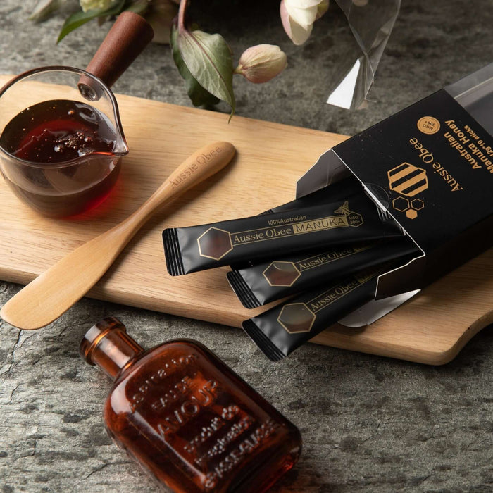 Manuka Honey MGO 300+ with sachets on a wooden board next to honey dipper and glass jar.